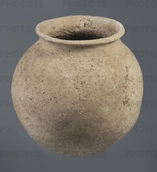 Spherical vessel, unknown Northern Mesopotamian workshop, Early Jazira III period ca. 2600–ca. 2350 BC Early Dynastic III period. Clay vessel; vice-less spherical vessel with rounded bottom. Upper part of the vessel wall bends inward, creating sloping arms that merge into an arched, low neck terminating in a narrow, outwardly obliquely cut rim with a triangular cross section. c. 2600–ca. 2350 BC. Northern Mesopotamia Khabur basin, Tell Rad Shakra Northeastern Syria. Vessel; height 20.3 cm, width 21 cm., A rounded clay vessel with a wide, slightly flared rim sits against a solid gray background; the vessel surface is rough and textured with an overall beige to light tan color, showing variations of darker brown and faint grayish areas, along with small pits and speckled spots; the interior appears darker and more shadowed, and the rim shows slight irregularities and wear.