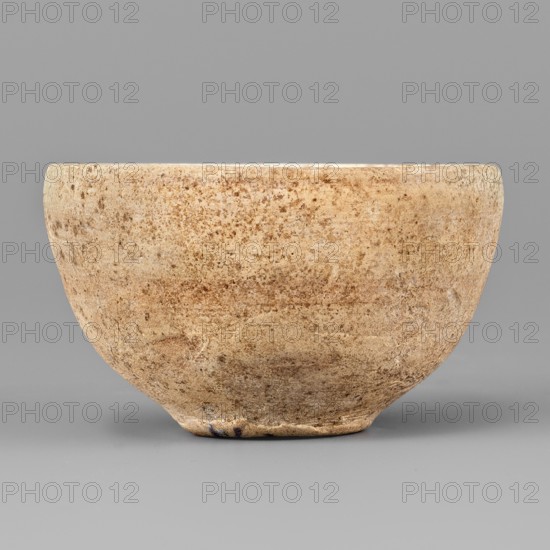 Bowl, unknown Northern Mesopotamian workshop; viseless, miniature clay vessel; flat, round, slightly distinct bottom with an arched bowl line terminating in a non-distinctive rounded rim. Early Jazira III period ca. 2600–ca. 2350 BCE, 1st half of 3000 BCE; Northern Mesopotamia Khabur basin, Tell Rad Shakra Northeastern Syria. Height 2.8 cm; width 4.9 cm., A weathered bowl with a rounded form and a slightly flattened base, showing a rough, pitted surface texture in shades of beige, tan, brown, and cream against a neutral gray background.