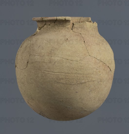 Spherical vessel, unknown Northern Mesopotamian workshop, Early Jazira III period ca. 2600–ca. 2350 BC / Early Dynastic III period ca. 2600–ca. 2350 BC. Spherical vessel with an egg-shaped belly and a rounded bottom. In the upper part the belly merges into a low cylindrical neck terminating in a narrow, strongly protruding, rounded rim turned outwards. Clay vessel; vice-free/bulbous vessel. c. 2600–ca. 2350 BC. Origin: Northern Mesopotamia Khabur basin, Tell Rad Shakra, northeastern Syria. Height 16.5 cm; width 16.2 cm., A rounded clay vessel with a wide rounded body and a short neck, showing visible cracks and repaired joins across its surface; the vessel is primarily beige with areas of light tan and subtle brownish and grayish patches, set against a solid medium gray background.