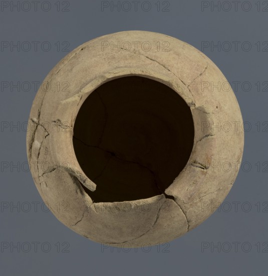Spherical vessel, unknown Northern Mesopotamian workshop, Early Jazira III period ca. 2600–ca. 2350 BC / Early Dynastic III period ca. 2600–ca. 2350 BC. Spherical vessel with an egg-shaped belly and a rounded bottom; in the upper part the belly merges into a low cylindrical neck terminating in a narrow, strongly protruding, rounded rim turned outwards. Clay vessel; vice-free bulbous vessel. c. 2600–ca. 2350 BC. Origin: Northern Mesopotamia Khabur basin, Tell Rad Shakra, northeastern Syria. Height 16.5 cm; width 16.2 cm., A round, broken clay vessel viewed from above with a large open mouth and visible cracks and missing fragments, showing a textured surface in shades of beige, tan, and light brown against a muted gray-blue background.
