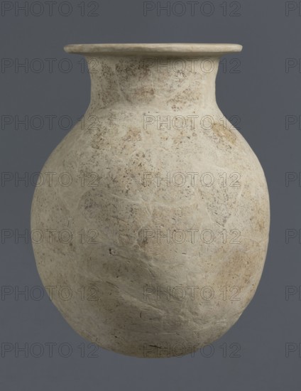 Vise-less jug, unknown northern Mesopotamian workshop, Early Jazira III period ca. 2600–ca. 2350 BC, clay, vise-less vessel. Bulbous ovoid belly with a flat, crookedly cut round bottom; sloping shoulders rising to a high cylindrical neck terminating in a wide, flat spout protruding outwards. Function: jug. Origin: Al-Jazira Northern Mesopotamia, Khabur basin; discovered at Tell Rad Shakra northeastern Syria., A large rounded ceramic vessel with a wide flat rim and a short neck, shown against a solid gray background, with an overall pale beige to off-white surface mottled with patches of light tan and subtle darker speckling, a textured surface showing irregular lighter veins and slightly rough areas, and shadows that emphasize its curved form.