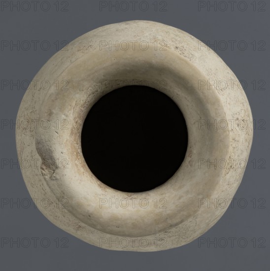 Vise-less jug, unknown northern Mesopotamian workshop; Early Jazira III period ca. 2600–ca. 2350 BC. Clay vise-less vessel: ovoid belly with a flat, crookedly cut round bottom, sloping shoulders, high cylindrical neck terminating in a wide, flat spout protruding outwards. Bulbous jug form; Early Dynastic III period; from Tell Rad Shakra, northeastern Syria Al-Jazira/Khabur basin, Northern Mesopotamia., A round, worn vessel with a wide circular opening shown from above, featuring a textured, uneven surface in shades of beige, off-white, cream, and light tan, with a deep black interior and a solid grey background.