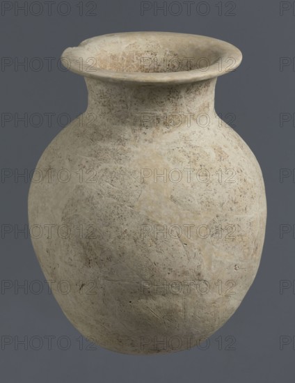 Vise-less jug, unknown northern Mesopotamian workshop; Early Jazira III period ca. 2600–ca. 2350 BC. Clay vessel: vise-less, bulbous jug with an ovoid belly, flat crookedly cut round bottom, sloping shoulders, a high cylindrical neck terminating in a wide flat spout protruding outwards. Function: vessel. Provenance/archaeological context: Tell Rad Shakra, northeastern Syria Al-Jazira/Khabur basin, Northern Mesopotamia; Early Dynastic III period ca. 2600–ca. 2350 BC., A large rounded vessel with a wide flaring rim, showing a textured surface with patchy wear and subtle scratches; the vessel displays a palette of light beige, cream, tan, and pale brown tones with darker speckling, set against a flat muted gray background.