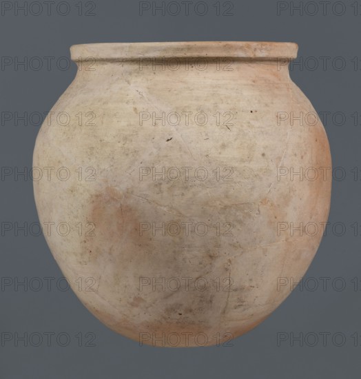 Spherical vessel, unknown northern Mesopotamian workshop, Early Jazira III period ca. 2600–ca. 2350 BC / Early Dynastic III period ca. 2600–ca. 2350 BC, clay, wheel-made, spherical vessel with an ovoid belly widening towards the top, small flat round bottom, short sloping shoulders merging into a low wide neck terminating in a rounded rim formed as a wide, thickened strip on the outside; provenance: Al-Jazira Khabur basin, northern Mesopotamia, Tell Rad Shakra Syria, northeastern Mesopotamia; height 28 cm, width 28 cm, A rounded clay vessel with a short, slightly flared rim sits against a solid background; the vessel shows a weathered surface with a few areas of pale beige, cream, light tan, and soft orange hues, along with subtle darker spots and smudges, fine surface cracks, and faint irregular texture across its curved body.
