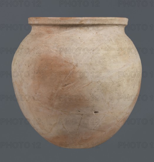 Spherical vessel, unknown northern Mesopotamian workshop, Early Jazira III period ca. 2600–ca. 2350 BC / Early Dynastic III period ca. 2600–ca. 2350 BC. Spherical vessel with an ovoid belly widening towards the top with a small, flat, round bottom, short sloping shoulders merging into a low, wide neck terminating in a rounded rim having the form of a wide, thickened strip on the outside. Clay vessel, vice-free, height 28 cm, width 28 cm. Origin: Northern Mesopotamia Khabur basin, Tell Rad Shakra, Syria northeastern Mesopotamia., A large rounded clay vessel with a short rim, showing a surface of muted beige and pale tan with areas of light reddish-brown and subtle grayish tones, visible texture and fine cracks across its body, small dark specks and a few tiny pits, set against a uniform dark gray background.