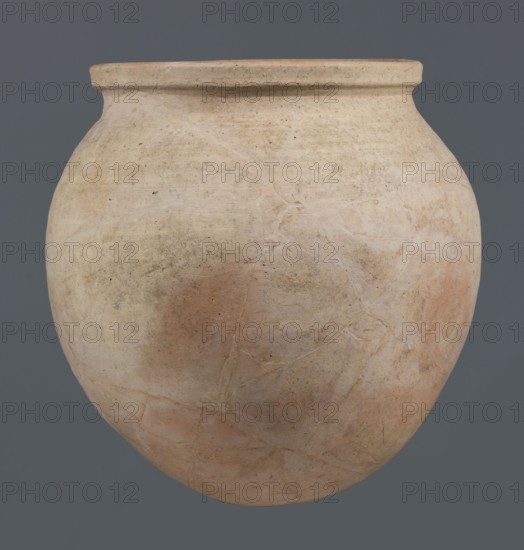 Spherical vessel, unknown northern Mesopotamian workshop, Early Jazira III period ca. 2600–ca. 2350 BC, Early Dynastic III period ca. 2600–ca. 2350 BC. Clay spherical vessel with an ovoid belly widening towards the top, small flat round bottom, short sloping shoulders merging into a low wide neck terminating in a rounded rim formed as a wide, thickened strip on the outside. Origin: Northern Mesopotamia Khabur basin, Tell Rad Shakra northeastern Mesopotamia, Syria. Height 28 cm; width 28 cm., A large rounded ceramic vessel with a wide rim, showing a weathered surface in shades of beige, cream, light brown, and pale terracotta, with several irregular lighter streaks and faint darker spots; the pot has a matte texture and visible fine cracks and subtle surface blemishes against a solid muted gray background.