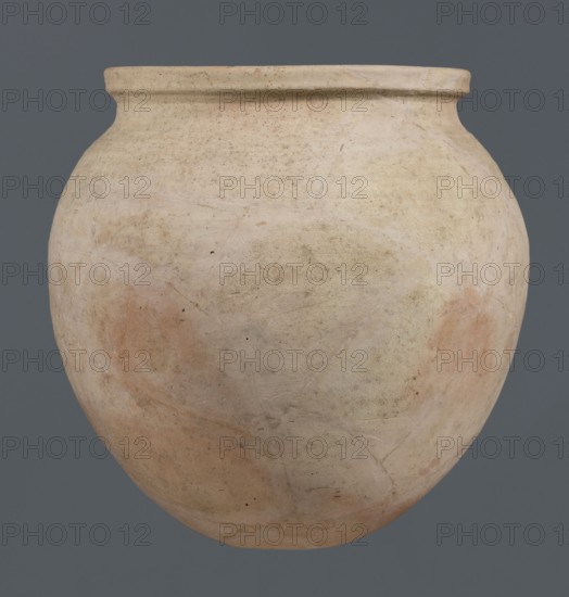 Spherical vessel, unknown northern Mesopotamian workshop, Early Jazira III period ca. 2600–ca. 2350 BC, clay, spherical vessel with an ovoid belly widening towards the top with a small, flat, round bottom, short sloping shoulders merging into a low, wide neck terminating in a rounded rim formed as a wide, thickened strip on the outside; ca. 2600–ca. 2350 BC; Early Dynastic III period; Al-Jazira Khabur basin, northern Mesopotamia, Tell Rad Shakra northeastern Mesopotamia, height 28 cm, width 28 cm., A large rounded ceramic vessel fills the frame, showing a smooth, bulbous body with a slightly flared rim; its surface displays a palette of beige, cream, off-white, pale pink, and light tan with subtle mottling and patches of reddish-beige, along with faint grayish and brown speckles and worn marks; the vessel has visible hairline cracks, small pits, and uneven texture, and it sits against a solid muted gray background.