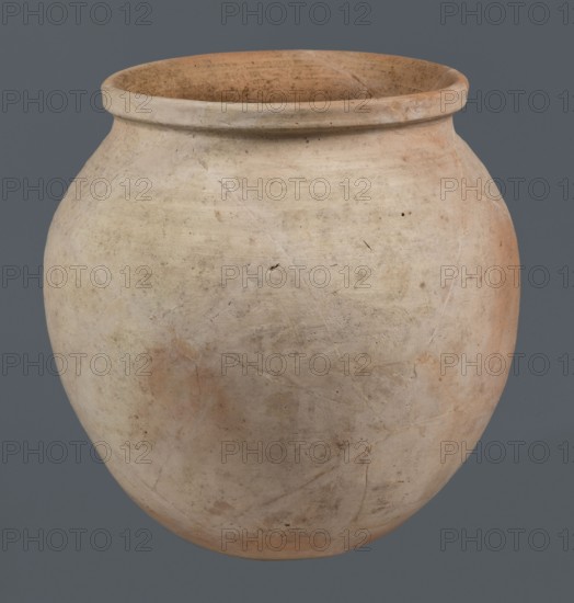 Spherical vessel, unknown northern Mesopotamian workshop, Early Jazira III period ca. 2600–ca. 2350 BC / Early Dynastic III period ca. 2600–ca. 2350 BC. Spherical vessel with an ovoid belly widening towards the top, small flat round bottom, short sloping shoulders merging into a low wide neck terminating in a rounded rim formed as a wide thickened strip on the outside. Clay vessel, vice-free, height 28 cm, width 28 cm. Origin: Northern Mesopotamia Khabur basin, Tell Rad Shakra, Syria., A rounded clay vessel with a wide open mouth and a slightly rolled rim sits against a solid gray background, showing an overall pale beige surface with patches of light tan and soft orange tones, subtle darker specks and smudges, faint surface cracks and lines, and a textured, slightly rough finish.