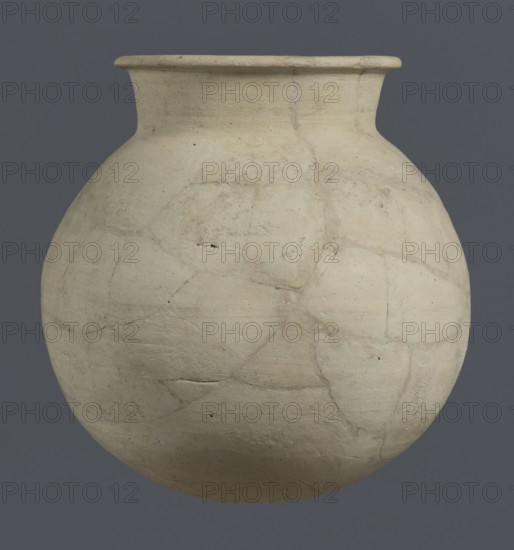 Globular vessel, unknown Northern Mesopotamian workshop; globular vessel, clay; excavations of the Centre of Mediterranean Archaeology, University of Warsaw; Early Jazira III period ca. 2600–ca. 2350 BC; vice-less vessels, children's graves; Al-Jazira Syria; Iraq; Mesopotamia; Early Dynastic III period ca. 2600–ca. 2350 BC; Globular vessel with a distinct, slightly flared conical neck ending with an outwardly extended and everted rounded rim; ca. 2600–ca. 2350 BC; Syria Northern Mesopotamia, Khabur basin, Tell Rad Shakra northeastern Syria; vessel; height 19 cm, width 18.2 cm, A large rounded clay vessel with a narrow neck and outward-flared rim sits against a solid gray background; the vessel surface is an off-white to beige color with visible repair lines and patchlike areas, showing a textured, slightly rough finish with faint discoloration in places and a few small dark specks.