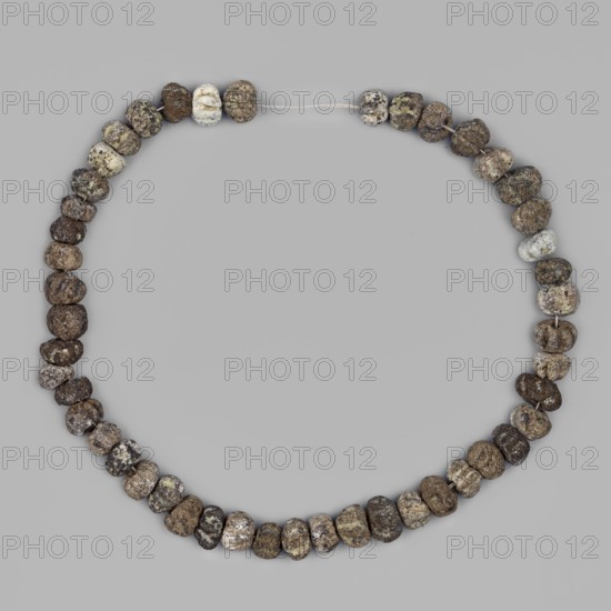 Necklace, unknown Northern Mesopotamian workshop; jewellery of frit beads; composed of forty-eight notched 6–7 notches spherical beads of medium size. Early Jazira III / Early Dynastic III period, 1st half of 3rd millennium BC c. 2600–c. 2350 BC. Northern Mesopotamia Khabur basin, Tell Rad Shakra northeastern Syria. Associated with children's graves as grave equipment. Decoration. Measurements: total length 29 cm; bead thickness min 0.44 cm, max 0.6 cm; bead diameter min 0.7 cm, max 0.96 cm; bead hole diameter 0.2 cm., A circular arrangement of small, irregular beads strung on thin thread against a plain light gray background, the beads showing rough, pitted surfaces and uneven shapes in a range of earthy colors including various shades of brown, beige, tan, gray, and some pale off-white, with a few beads appearing speckled or mottled and the thread visible at the top where two beads are slightly separated.