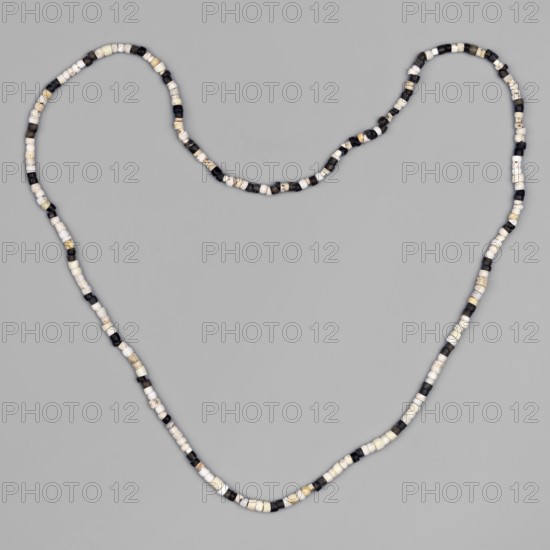 Necklace composed of 268 small beads cylindrical and discoid in white and black stringing and composition are contemporary. Necklace of small beads. Beads; jewelry; decoration. 1st half of the 3rd millennium BC; Early Jazira III period c. 2600–c. 2350 BC. Northern Mesopotamia, Khabur Basin, Tell Rad Shakra northeastern Syria. Height 51 cm., A long strand of small cylindrical beads arranged in a loose heart-like loop against a solid background, the beads alternating in a pattern of white, black, and beige tones with a few beads showing mixed or speckled coloration, the background appearing a uniform light gray.