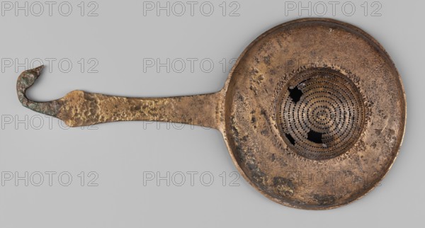 Strainer with a handle in the form of a swan's head;, swans iconography; tools. Wide, flattened container with a hemispherical strainer and a flat handle ending in a bird's head. 2nd half of the 4th century BC. Etruria. Vessel. Height 23.1 cm; width 11.3 cm; depth 4 cm; weight 0.14 kg., A flat metal object with a long handle and a round, shallow bowl is shown against a pale gray background; the metal surface is mottled with brown, dark brown, and bronze tones with areas of darker corrosion and some greenish-blue patina near the curled end of the handle, the handle itself is textured and tapers to a hooked curled tip, and the bowl has a concentric perforated pattern at its center with a few irregular missing sections and rough, pitted edges.