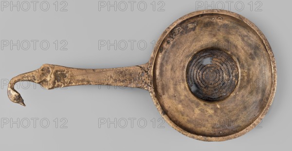 Strainer with a handle in the form of a swan's head;, swans iconography; tools. Wide, flattened container with a hemispherical strainer and a flat handle ending in a bird's head. 2nd half of the 4th century BC previously dated 4th century BC. Etruria. Vessel. Height 23.1 cm; width 11.3 cm; depth 4 cm; weight 0.14 kg., A single metal object resembling a shallow bowl with a long handle is shown against a plain gray background, the object displaying a weathered metallic surface in shades of gold, bronze, brown, and darker tarnished areas; the bowl has a circular recessed center with a patterned perforated disk that appears darker with black and deep brown tones, and the rim and interior show mottled patches of lighter and darker bronze; the handle extends outward with an irregular hooked end and a textured, pitted surface in bronze and gold hues, and the overall piece has an aged, uneven finish with small spots of darker discoloration.