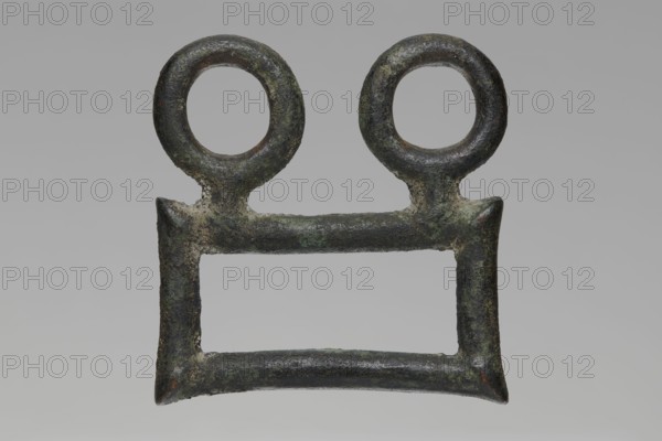 Buckle, Bronze buckle consisting of two parts in a shape similar to rectangles with joints. One part has hooks in the form of zoomorphic decoration animal heads. 7th century BC, Etruria. Decoration. Length 13 cm total; height 7.5 cm; thickness 4 cm; weight 0.374 kg; length 7.2 cm single element., A weathered metal object with a rectangular open center and a horizontal bar across the top, topped by a pair of circular loops; the surface shows rough, pitted texture and corrosion with visible patches of green, dark brown, gray, and black.