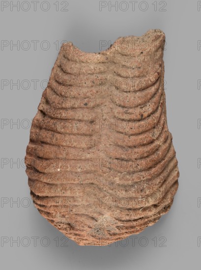 Votive offering in the form of a womb, votive offering, Ex-voto in the form of a womb, 332–30 BC; Hellenistic period, Caere place of origin, votive offering, height 4.5 cm, length 13.2 cm, width 9 cm, weight 0.27 kg, An irregularly shaped, weathered object with layered, ribbed surface texture and undulating horizontal ridges, primarily in shades of reddish-brown and tan with small darker speckles, set against a plain light gray background.