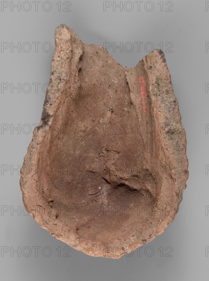 Votive offering in the form of a womb;, votive offering, body part ex-voto in the form of a womb; 332–30 BC, Hellenistic period; Caere place of origin; terracotta, ; height 4.5 cm, length 13.2 cm, width 9 cm, weight 0.27 kg., A roughly oval, broken clay object with uneven, craggy edges and a concave interior, showing a textured, gritty surface in shades of reddish-brown and tan with small darker specks; the piece has irregular raised rims on two sides and an area of rougher, more weathered outer surface, all set against a flat gray background.