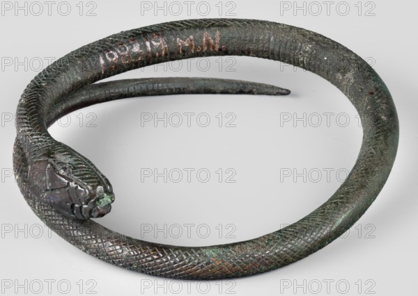 Bracelet. Made of flattened wire with thinning, overlapping ends. 9th–8th century BC; Villanovian period, Etruria. Body ornament; weight 46 g; height 1.2 cm; diameter 8.5 cm., A coiled metal object shaped like a snake with textured, scale-like patterning along its body and a stylized head at one end, shown resting on a light neutral surface; the object displays a mottled patina with visible shades of dark green, brown, and hints of black and copper, and there are small areas of lighter green corrosion on the surface.