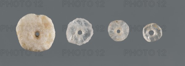 Set of four disc-shaped beads of different sizes, unknown northern Mesopotamian workshop, Al-Jazira Syria/Iraq, Mesopotamia, beads, disc-shaped beads, jewellery, used in children's graves, ca. 2600–ca. 2350 BC Early Jazira III period / Early Dynastic III period, Northern Mesopotamia Khabur basin, Tell Rad Shakra Northeastern Syria, decoration, A horizontal row of a few round, donut-shaped translucent objects rests against a solid gray background, each object varying in size and texture; the leftmost piece is larger, off-white with pale yellowish and beige mottling and a small central hole, the next pieces are smaller and more translucent with clear to milky white tones and some cloudy inclusions, while the rightmost items are the smallest, showing clear to whitish translucency with faint brownish spots and irregular edges.