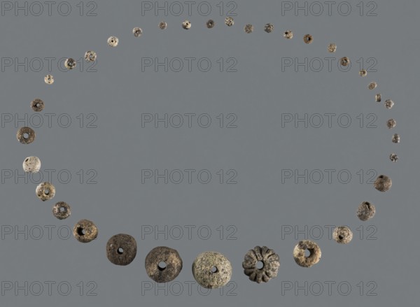 Necklace, unknown northern Mesopotamian workshop, Early Jazira III period ca. 2600–ca. 2350 BC, jewelry. Necklace composed of 35 beads of various shapes and sizes: one large spherical fluted bead flattened on one side 1, three large spherical beads slightly flattened at both ends 2–4, two large cylindrical beads 5–6, three medium circular beads 7–9, five small biconical beads 10–14, two small cylindrical beads 15–16, and nineteen small cylindrical beads 17–35. Round beads correspond to segments of a sphere. Bead size categories: small = 0.35 cm; small > 0.35 cm and < 0.5 cm; medium > 0.5 cm and = 1 cm; large = 1 cm. ca. 2600–ca. 2350 BC; found at Tell Rad Shakra northeastern Syria, Northern Mesopotamia Khabur Basin. Decorations include biconical, cylindrical, spherical, and fluted beads; associated with children's graves., A circular arrangement of many small round objects on a flat background, forming a ring with a clear central empty space; the objects vary in size and texture, some ...