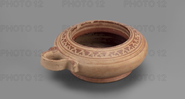 Exaleiptron kothon on a low, conical foot. Ribbon-shaped base, upper part covered with varnish. Band decoration painted on clay. Delicate lines painted in red. Decoration in the form of concentric circles on the bottom of the vessel. Delicate orange lines. Main decorative ornament consists of smaller, narrower leaves. Outer part of the foot covered with red varnish. Inner surface entirely covered with red varnish thin, unevenly distributed layer. Technology: Smooth surface. Visible traces of turning. Fine-grained clay, visible pyroxene. Notes: Glued artefact. Conservation work visible. Large losses in varnish and impurities visible inside the vessel. Clay color: Red 10 R 5/4 weak red — 10 R 5/8 red. Attributed maker: unknown. Date: 2nd half of the 6th century BC. Place of origin: Corinth. Object type: vessel, kothon, exaleiptron. Dimensions: height 5.5 cm, width 17.4 cm, depth 14.5 cm, weight 0.304 kg., A shallow round ceramic vessel with a short spout-like handle on one side, showing ...