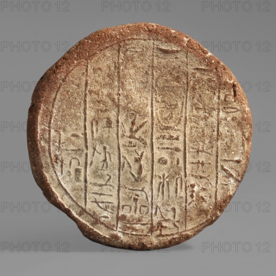 Rames's funerary cone, funerary cone with 6 impressed columns of hieroglyphic inscription, cartouches, hieroglyphs; maker, ca. 690–664 BC Third Intermediate Period, 25th Dynasty, reign of Taharqa; Western Thebes grave 132; grave goods; cone, weight 0.5 kg., A circular, flat object with a rough, textured surface showing carved linear grooves and shallow incisions arranged in vertical columns, displaying worn pictorial marks and shapes. The object has an overall earthy brown and beige coloration with lighter beige in the recessed carved areas and a darker reddish-brown along the rim and outer edge. The surface appears weathered with small pits and chips and variations in tone, and the background is a smooth neutral gray.