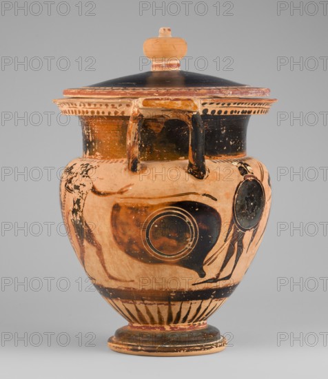 Column krater with lid, unknown Attic workshop, Black-figure krater with lid. Red clay, tinted with ochre. Black firnis with a muted lustre, fading to brown in places. The rim of the vessel is decorated with a radial ornament and a schematic ivy sprig. On the shoulders are a series of vertical lines. The belly is decorated with figural scenes. On side A, Dionysus with a cornucopia is visible, accompanied by a Satyr and a Maenad. On side B an archer is shown between two helmeted hoplites with round shields. A lid with a pomegranate-shaped handle, decorated with an ivy sprig placed on the rim. 520–510 BC, Attica. Vessel: column krater. Weight 1.382 kg; diameter 19.2 cm 22.5 cm with vices; height 21.4 cm 22.6 cm with vices., An earthenware vessel with a lid, shown against a plain gray background, featuring a rounded body, a flared rim with a flat lid topped by a small knob, and a short pedestal base; the vessel displays a worn painted decoration in shades of orange, terracotta, black, and...