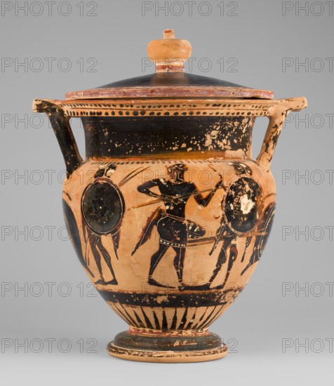 Column krater with lid, unknown Attic workshop. Black-figure krater with lid. Red clay, tinted with ochre; black firnis with a muted lustre, fading to brown in places. Rim decorated with a radial ornament and a schematic ivy sprig; shoulders with a series of vertical lines. Belly decorated with figural scenes. Side A: Dionysus with a cornucopia accompanied by a satyr and a maenad. Side B: an archer flanked by two helmeted hoplites with round shields. Lid with a pomegranate-shaped handle, decorated with an ivy sprig on the rim. Circa 520–510 BC, Attica. Vessel type: column krater. Weight 1.382 kg; diameters 19.2 cm body and 22.5 cm with vices; heights 21.4 cm body and 22.6 cm with vices., An orange terracotta vessel with a lid and two handles sits against a neutral gray background; the vessel shows black painted figures and decorative bands, with visible wear and flaking revealing the base orange color beneath; a group of black-figure human silhouettes and shields encircles the body, ea...