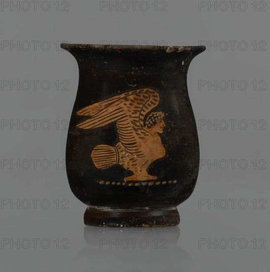 Jug, red-figure pottery, Greek, mermaid mythological, Athens, 3rd quarter of the 5th century BC, Attica; vessel, height 6.6 cm. A small jug with a low foot recessed at the bottom. The edges of the foot are slightly rounded and tapered upwards. The body is slightly wider than the foot, rounded at the bottom, almost cylindrical in the lower half, and gently tapering in the upper half, merging into a widely flared outward spout. Below the spout is a vertically mounted, cylindrical, slightly flattened handle, bent into a circle. Light orange clay with black, shiny slip. On the body, the mermaid is in right profile, with wings raised upwards the left wing at the back, protruding above the right. On the mermaid's head is a diadem marked with white dots. Feathers are marked with lines—long and thin at the wingtips and tail; thin and thick elsewhere. The image is emphasized from the bottom with a row of dots. The side of the foot is chipped, the rim edge is slightly chipped, and the slip shows...