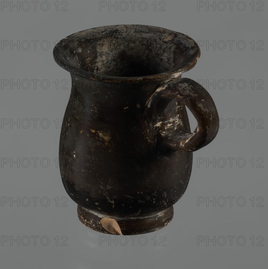 Jug, red-figure pottery, Greek pottery, mermaid mythological, Athens Greece. A small jug with a low foot recessed at the bottom. The edges of the foot are slightly rounded and tapered upwards. The body is slightly wider than the foot, rounded at the bottom, almost cylindrical in the lower half, and gently tapering in the upper half, merging into a widely flared outward spout. Below the spout is a vertically mounted, cylindrical, slightly flattened handle, bent into a circle. Light orange clay, black, shiny firnis. On the body, the mermaid is in right profile, with wings raised upwards the left wing at the back, protruding above the right. On the mermaid's head is a diadem marked with white dots. Feathers marked with lines—long and thin at the wingtips and tail; thin and thick elsewhere. The image is emphasized from the bottom with a row of dots. The side of the foot is chipped, the rim edge is slightly chipped, and the firnis is abrasion-stripped. Part of the rim is filled with plaster...