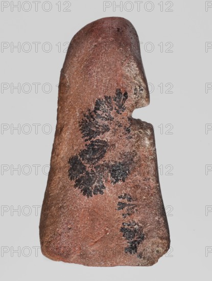 Mold for a figurine of the goddess Isis, maker, Isis myth., Egyptian deities, Egyptian religion, crowns; 664–332 BC, Late Period, Egypt; mold; height 2.5 cm, width 5.1 cm, depth 3.4 cm, A roughly triangular, weathered stone with a rounded top and a notched side, showing a predominantly reddish-brown surface with patches of lighter tan and gray; several dark black, fern-like dendritic patterns appear across the front face, contrasting with the surrounding rusty and muted pinkish tones, and the texture looks coarse and grainy.