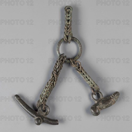 Pendant with phalluses, phalluses, pendants, amulets - body parts, 1st century, Italy, amulet, weight 50 g, An object consisting of a circular ring with two braided chains hanging from it, each chain ending in a small metal pendant shaped with rounded and elongated forms; the metal shows a patina with greenish and brownish tones and darker gray areas, and the background is a uniform light gray.