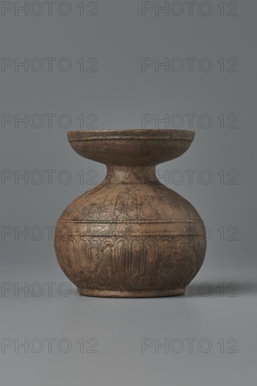 Aryballos, 2nd–1st century BC; Sicily Segesta?; Etruria ; vessel aryballos; weight 0.11 kg; height 5.4 cm; diameter 5 cm., A rounded vessel with a flared lip and a narrow neck sits centered against a smooth background; the object appears textured and worn with carved vertical and scalloped decorative bands around its bulbous lower body and a raised rim at its base. The visible colors include shades of brown and dark bronze with areas of darker patina and subtle hints of black, set against a flat gray backdrop.