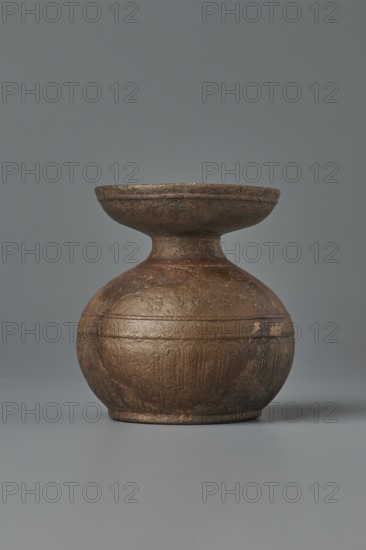 Aryballos, 2nd–1st century BC, Sicily Segesta - incorrect information?, Etruria, vessel aryballos, weight 0.11 kg, height 5.4 cm, diameter 5 cm, A round, textured vessel with a bulbous base and a flaring, shallow rim sits centered against a plain backdrop; the surface of the vessel shows an uneven, rough texture with visible worn areas and a banded groove encircling the midsection, and the colors visible are brown with darker brown and subtle reddish-brown variations, set against a gray background and a gray surface beneath it.
