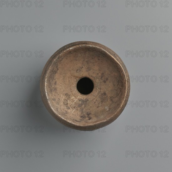 Aryballos, 2nd–1st century BC, Sicily Segesta? incorrect information?, Etruria possible origin, vessel aryballos, weight 0.11 kg, height 5.4 cm, diameter 5 cm, A round, bowl-shaped object viewed from above with a central circular hole, showing a textured, worn surface in shades of brown and tan with darker brown spots and patches, resting on a smooth background in shades of gray and bluish-gray, with subtle shadowing beneath the object.