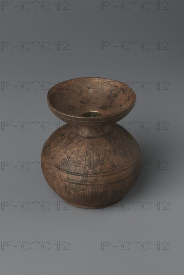 Aryballos, 2nd–1st century BC, Sicily Segesta - incorrect information?, Etruria, vessel aryballos, weight 0.11 kg, height 5.4 cm, diameter 5 cm, A single rounded vessel with a wide flared rim and a narrow neck connecting to a bulbous body sits on a flat surface; the surface of the vessel shows textured, weathered patina with irregular dark patches and worn areas, and faint incised decorative bands and vertical motif-like grooves encircle the lower body. The vessel displays brown and coppery tones with darker brown and black mottling and subtle greenish hints in spots, and the background and surface beneath the vessel are neutral gray.