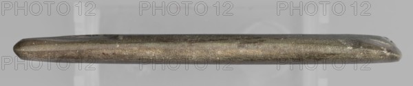 Rectangular paddle with a hole at one of the shorter edges; possibly a whetstone. Flat rectangular paddle, geometric design. Predynastic Period Naqada III phase, 2nd half of the 4th millennium BC, Egypt. Paddle; height 8.2 cm, width 11.1 cm, weight 0.174 kg., A long narrow metallic object is shown horizontally against a light gray background, with rounded tapered ends and a slightly irregular surface texture; the object displays a mix of dull metallic colors including shades of gray, bronze, and brown with small lighter flecks and subtle darker streaks along its length.