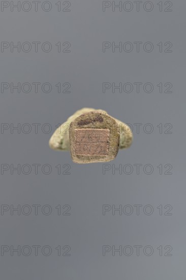 Ushabti ?-en-Khonsu, Mummy-shaped figurine shabti. Arms crossed on the chest, the right folded over the left, holding hoes in both hands with convex tools. Rectangular low basket on the back. Smooth tripartite wig, large ears, facial details poorly legible. Wig, facial details and basket painted black. Painted inscription in a framed column on the front of the legs: Osiris the god father of Amun, Waad, -en-Khonsu, scribe, justified by the voice. c. 1069–c. 945 BCE; Third Intermediate Period, 21st Dynasty, Egypt. Height 12.7 cm., A small, irregularly shaped object with a rough, textured surface in shades of beige, tan, and light brown is centered against a uniform gray background; the object shows a rectangular patch of woven fabric in a muted pinkish-beige tone embedded on one face and a darker brown smudge near the top edge, with subtle speckles of greenish and darker brown across its surface and soft shadows suggesting slight elevation from the background.