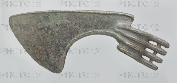 Battle axe, unknown Luristan workshop. Battle axe with a low cylindrical socket with a round hole, from which grows a blade terminating in a semicircular cutting edge set at ~45° to the axis of the shaft. The base of the blade protrudes above the socket; its upper edge is sloping and straight with a slight bulge in the middle, while the lower edge is shorter and slightly obtuse arc-shaped. Four identical blunt-tipped spikes project from the butt, connected vertically at mid-length; the spikes extend into side ribs on both sides of the socket — the upper two terminate at the blade base, the third extends into its lower edge, and the fourth runs around the lower edge of the socket, reinforcing it. Luristan, Iran; 2nd half of the 2nd millennium BC. Weapon. Weight 334 g; height 10.2 cm; length 19 cm; thickness 3.2 cm., An aged metal object with a broad, roughly triangular blade area showing a mottled surface in dark gray, brown, and patches of green, connected to a curved neck that leads t...