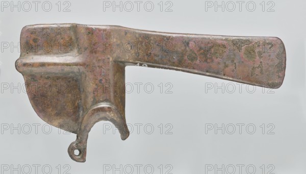 Battle axe, Eastern Gallic Scenography, 2nd half of 3rd millennium BC, Western Iran, weapon, weight 280 g, An aged metal tool with a patinated surface in shades of brown, green, and pinkish tones, showing spots of darker and lighter wear; the object has a long flat tapered arm extending to one side and a rounded, thicker body at the other side with a curved hook-like projection ending in a small open loop; the metal surface shows mottled corrosion, textured pits, and smooth worn areas against a pale neutral background.