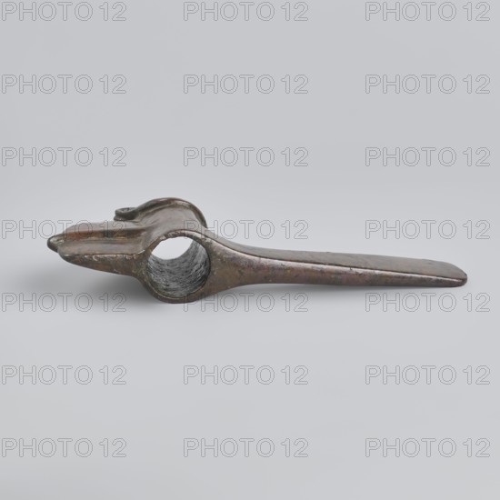 Battle axe, Eastern Gallic Scenography, 2nd half of 3rd millennium BC, Western Iran, weapon, weight 280 g, A single elongated metallic object rests on a light gray background, showing a worn, slightly curved form with a hollow circular opening near one end and a flattened tapered end at the other; the surface displays a mottled mix of dark bronze, brown, and hints of green patina with areas of darker gray inside the hollow and subtle shiny reflections on the outer surfaces.