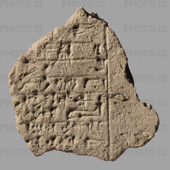 Brick fragment with Gudea's foundation inscription, Gudea ca. 2150 BC, architectural element in clay with cuneiform writing, Near Eastern Sumerian architecture, 2nd Dynasty of Lagash ca. 2150 BC, provenance: Girsu/Tello Sumer, Iraq, foundation inscription, weight 1.35 kg, A roughly triangular fragment of a textured beige stone slab sits against a flat gray background, its surface pitted and worn with shallow rectangular impressions and linear grooves arranged in horizontal groupings; the edges are irregular and chipped, showing rough, crumbled areas and small hollows, and the stone displays subtle variations of tan and light brown tones with faint shadows accentuating the carved depressions.