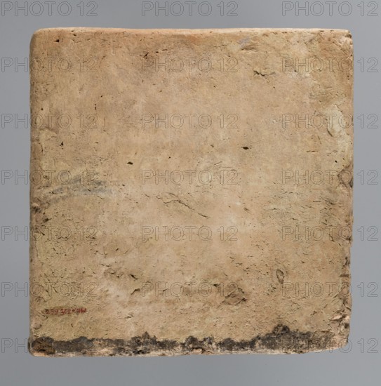 Brick with an inscription of King Shalmaneser III, Shalmaneser III 858–824 BC Shulmanu-ašared, king of the Neo-Assyrian Empire. Calah Iraq, the ziggurat at Kalhu Nimrud. Square brick with cuneiform inscription: the upper surface is inscribed over almost its entire surface with seven lines of carefully impressed cuneiform characters. Sand-colored clay, one edge burnt to black. Date: 858–824 BC. Place of origin: Kalhu Nimrud. Material: brick. Weight 20.97 kg; width 35 cm; length 35 cm; thickness 12 cm., A roughly square, flat object with a textured, worn surface in shades of beige, tan, and light brown, showing irregular pits, small cracks, and rough patches; the edges are rounded and slightly darker, with a darker border along the bottom edge that appears smudged in shades of gray and black; the background behind the object is a smooth, neutral gray.