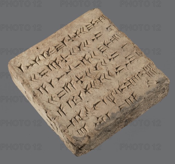 Brick with an inscription of King Shalmaneser III, Shalmaneser III 858–824 BC Shulmanu-ašared, king of the Neo-Assyrian Empire. Origin: Calah Kalhu/Nimrud, the ziggurat at Kalhu. Square brick inscribed over almost its entire upper surface with seven lines of carefully impressed cuneiform characters. Sand-colored clay, one edge burnt to black. Date: 858–824 BC. Material: brick. Weight: 20.97 kg. Dimensions: width 35 cm, length 35 cm, thickness 12 cm., A rectangular clay tablet with a rough, uneven surface in shades of beige and light brown rests against a gray background; the tablet's top is covered with rows of wedge-shaped incisions forming repeated angular markings, and its edges and corners are chipped and worn exposing darker brown and gray patches.