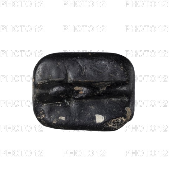 Rectangular stamp seal with a handle in the form of a protruding ridge along the axis of the seal with a crosswise drilled hole. On a rectangular base with rounded corners is a schematic representation of a demon, in human form and with wings instead of arms. Unspecified filler elements are on the sides of the demon. c. 1650–c. 1350 BC; Late Bronze Period. Northwest Syria place of manufacture, Near East place of find. Material: seal. Dimensions: height 1.7 cm, width 4.2 cm, depth 3.2 cm., A dark rounded rectangular object with a smooth, slightly worn surface showing a few rough patches and chips in lighter tones; the object is primarily black with small areas of gray, off-white, and beige where the surface is worn away, and it has shallow carved or indented grooves across its face giving it a segmented appearance.