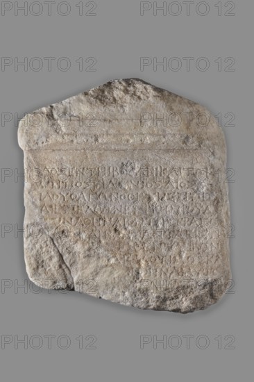 Greek honorific inscription, unknown Greek workshop,  creator, decrees, Hellenistic period, cities, Greek inscriptions, actors, Stele topped with a tympanum, separated from the epigraphic field by moldings. Eleven lines of Greek text preserved, partially damaged, especially on the right and left edges. The text was longer, the lower part of the object is missing. The back side is unworked. Greek honorific inscription with a decree from Perinthus in honor of the tragic actor Athenaios. 300–250 BC, Perinthus, Greek inscription, height 38 cm, width 25.5 cm, thickness 18 cm, weight 16.2 kg, A roughly rectangular stone slab with an irregular top edge and rounded corners resting against a neutral gray background; the stone's surface is textured and weathered with an overall palette of beige, light brown, off-white, and gray tones, with darker gray and brown patches and some faint white mineral deposits; shallow carved lines and incised areas are visible across the face of the slab, creating ...