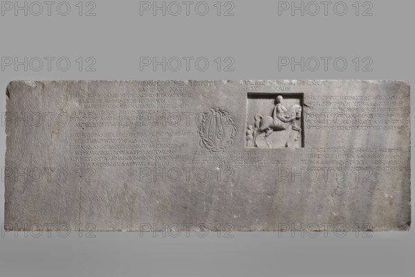Family tombstone with epitaph, unknown workshop, Greek inscriptions, restitution Braniewo ; Lyc.Hosianum, sepulchral funerary architecture, riders iconographic, wreaths, laurel wreaths, ribbon ornament, horses iconographic, sepulchral sculpture artist, rectangular marble slab, diagonally cracked. The block bears an inscription divided into three parts and two reliefs - a laurel wreath with a ribbon and a metope with a depiction of a young man on horseback accompanied by a slave . Both faces are damaged - perhaps hammered. The rider is dressed in a chiton and chlamys. The slave is exaggeratedly reduced in size in relation to the rider. He is dressed in a short girded chiton and holds a spear in his hand. 1st century BC - 1st century AD, Cyzicus, Asia Minor, Greek inscription, grave inscription, stele, gravestone, bas-relief, height 76 cm, width 203 cm, depth 11 cm, weight 450 kg, A rectangular stone slab with a rough light gray surface showing a shallow rectangular recess on the right t...