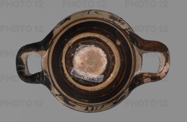 Miniature skyphos. Reddish clay, black-brown firnis poorly covering the outside on the foot, at the bottom of the body, the outer parts of the handles, the rim and the inside. The zone between the handles is white-ground, black-figure. Decoration: A - seated human figure in right profile; B - standing human figure facing right and quadruped facing left. Black-figure pottery, white-ground technique; miniature vessel, skyphos; Attic, Athens, 1st quarter of 5th century BC. Height 4 cm, width 5.2 cm. Creator, Attic workshop unknown., A top-down view of a small two-handled ceramic vessel with a rounded body and a central circular base, showing worn and chipped surfaces. The vessel has broad concentric bands of dark brown and beige around the interior rim and base, and the handles are dark brown with beige worn areas. There are areas of pinkish beige on the central base and small patches of white residue near the center and along some chips. The background is a uniform grey.