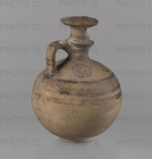 Cypriot jug, painted pottery, Jug with a flat foot, spherical body, high narrow neck with a strongly tilted spout, and a small vertical handle supported by arms and a ring on the neck. Above the maximum diameter: a black band and a set of five parallel lines framed by thicker bands. On the arms: four sets of concentric circles arranged symmetrically on the sides of the vessel's axis. Handle decorated with transverse lines. 850–750 BC; Cypriot — Geometric Period III. Cyprus. Vessel, jug. Height 10.5 cm, width 7.8 cm., A round ceramic vessel with a single curved handle and a narrow neck topped by a flared rim, showing a worn surface with visible chips and rough areas; the body is decorated with concentric banding and circular motifs, and the piece rests on a small rounded foot. The visible colors include beige, light brown, darker brown, gray, and hints of reddish-brown.