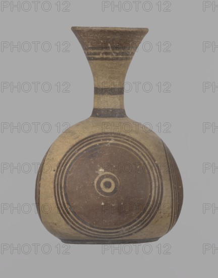 Cypriot jug, Jug on a low, straight foot. Globular body, flattened at the bottom. Quite narrow neck, funnel-shaped spout. Slightly flattened handle attached to the base of the neck and the upper part of the body. Painted decoration in stripes and linear patterns, in red-brown and black fading to brown. Near the spout is a wide red band, below it three black lines, the first adjacent to the red band. At the lower part of the neck, above the handle attachment, a narrow black band; another narrow black band at the base of the neck. The belly is decorated with three identical shooting target motifs on the front and sides: a wide red circular band with a black dot and a circle in the center, surrounded by four black-brown circles, the first adjacent to the red band. The handle is unpainted on the vessel side, black on the top, with light horizontal lines. The foot on the side is black. On the bottom, two concentric circles with a center marked with a dot. Good condition. Cypriot, Geometric ...