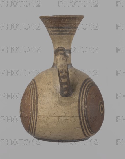 Cypriot jug, Jug on a low, straight foot. Globular body, flattened at the bottom. Quite narrow neck, funnel-shaped spout. Slightly flattened handle attached to the base of the neck and the upper part of the body. Painted decoration in stripes and linear patterns, in red-brown and black fading to brown. Near the spout is a wide red band, below it three black lines, the first adjacent to the red band. At the lower part of the neck, above the handle attachment, a narrow black band; another narrow black band at the base of the neck. The belly is decorated with three identical shooting target motifs on the front and sides: a wide red circular band with a black dot and a circle in the center, surrounded by four black-brown circles, the first adjacent to the red band. The handle is unpainted on the vessel side, black on the top, with light horizontal lines. The foot on the side is black. On the bottom, two concentric circles with a center marked with a dot. Good condition. Cypriot, Geometric ...